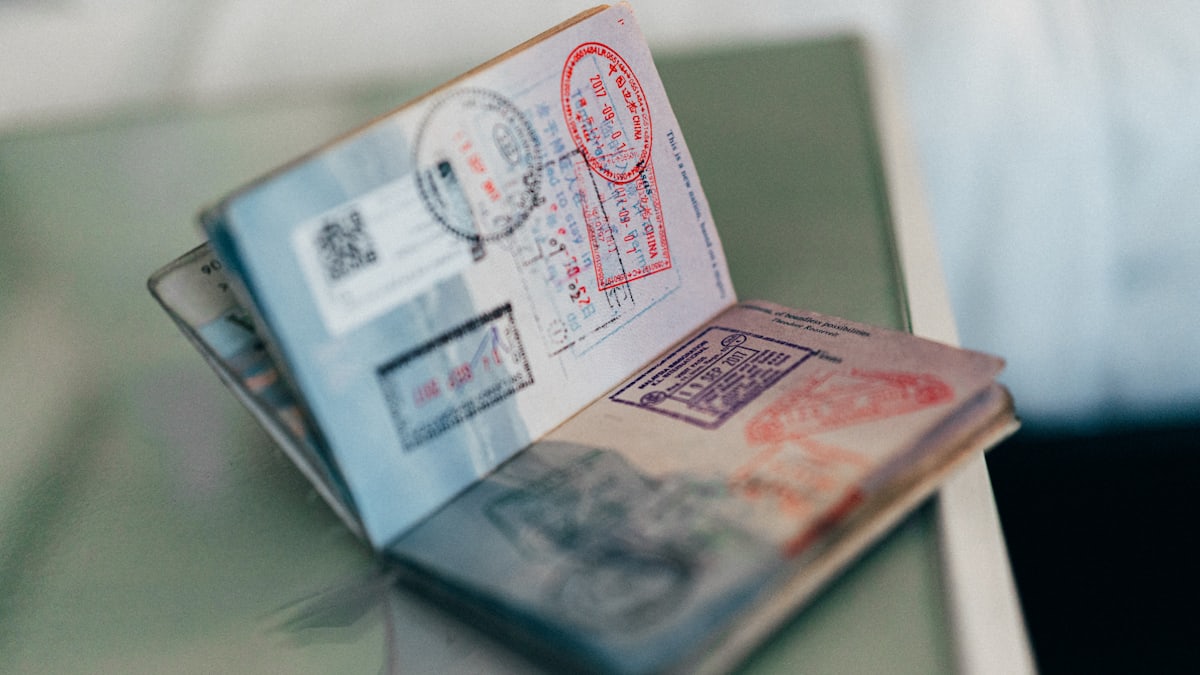 A close-up of a blue passport resting on official-looking paperwork with various stamps.