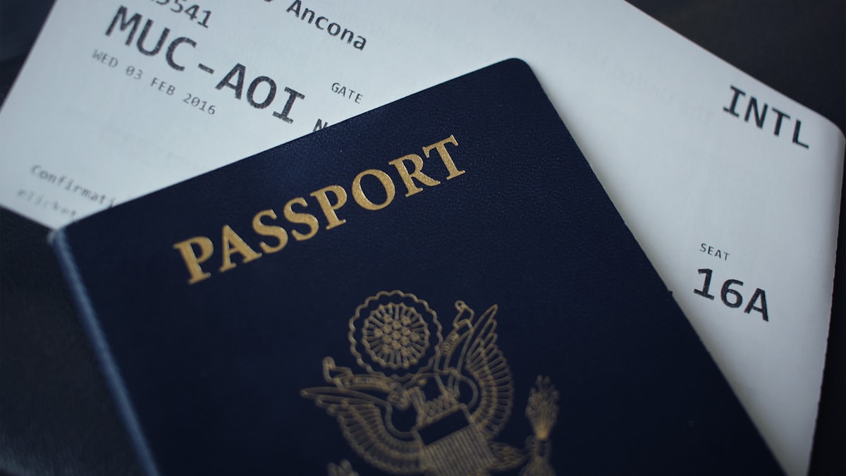A person holding a passport and a wallet with several credit cards while standing in an international airport terminal.