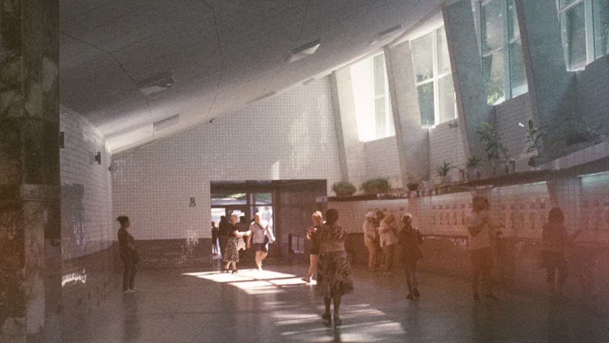 A parent holding a young child's hand as they walk towards a school building entrance on a crisp morning.